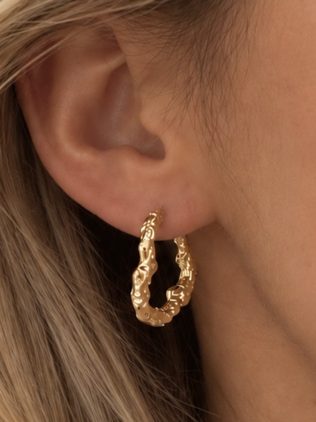 Roé guldørering — textured hoop i close-up på model med blondt hår foran varme julelys